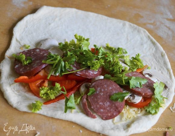 Один край смазать томатной пастой, выложить немного сыра, помидоров, перец чили и болгарский, затем шампиньоны, зелень и колбасу. Обильно посыпать сыром Джюгас.