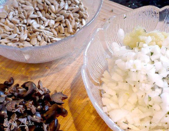 Ставим вариться картофель в мундире в небольшом количестве воды до готовности, т.е. минут на двадцать. Разогреваем духовку до 200 градусов. Семечки поджариваем на сухой сковороде. С веточек розмарина снимаем иголочки и мелко рубим их. Лук и оливки режем мелко. Чеснок натираем на мелкой терке. 