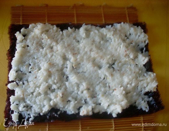 Распределить рис по листочку нори, стараясь выкладывать не слишком  толстым слоем.