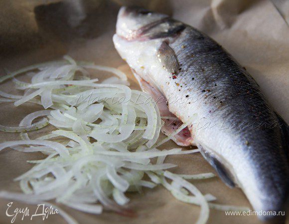 Рыбу почистить, разрезать по брюшку до конца головы, вытащить всё не нужное изнутри, жабры. Я не люблю, когда в готовом блюде есть глаза, поэтому их тоже убираю. Рыбу как следует помыть снаружи и изнутри. Натереть солью и смесью перцев. В форму выложить пекарскую бумагу или пергамент. Лук нарезать очень тонкими полукольцами и выстелить на дно формы. Сверху на луковую подушку положить рыбу. 