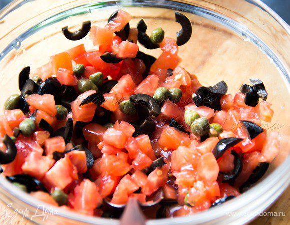 Томаты разрезать, достать семечки. Мякоть нарезать на небольшие кубики. Вытащить из оливок косточку и произвольно нарезать. Смешать в миске томаты, оливки и каперсы. Несильно посолить, добавить орегано и базилик. 