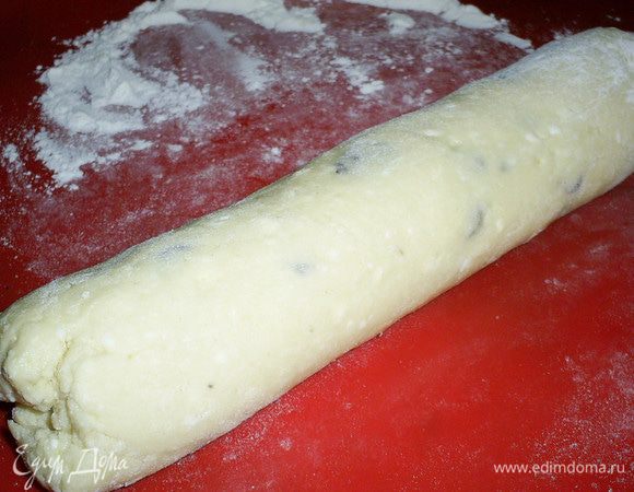 Добавляем муку, просеянную вместе с содой. Замешиваем тесто. Оно не должно быть слишком крутым и будет немного липнуть к рукам. Выкладываем часть теста на стол, посыпанный мукой и раскатываем колбаску диаметром около 5 см.