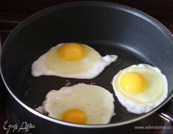 Убираем хлеб со сковороды, вытираем ее бумажной салфеткой и пожарим 2-3 яйца, каждое отдельно, чтобы не соприкасались. Готовим их 6-7 минут, так чтобы желток остался жидким.
