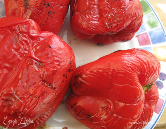 Наколоть сырые перцы вилкой. Разогреть духовку до 200 градусов. Положить в нее на противень перцы, через некоторое время  перевернуть перцы, чтобы не пригорели. На запекание уйдет минут 20.  Выключите духовку, оставьте там перцы, пока они не остынут.  
Можно воспользоваться другим методом: разогреть духовку до 250 градусов в режиме гриль, у перца удалит плодоножку, разрезать на четыре части каждый перец, извлечь семена и положить перец срезом вниз, смазать  наружную часть перца оливковым маслом. Поставить в духовку на 5 минут или до тех пор, пока кожица не пойдет пузырями.

