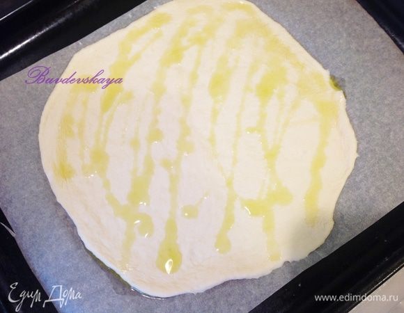 Тесто поделите на 2 части. Возьмите 1 часть теста и сформируйте круглую основу для пиццы руками или скалкой. Выложите на противень, застеленный пергаментом. Сбрызните пиццу оливковым маслом и равномерно распределите его по тесту. То же самое повторите со второй частью или оставьте ее на потом.