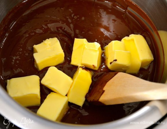 Тем временем, шоколад поломать на кусочки и поставить плавиться на водяной бане. Как только шоколад растает, добавить 100 г сливочного масла кусочками и как следует размешать. Отставить в сторону остывать.

