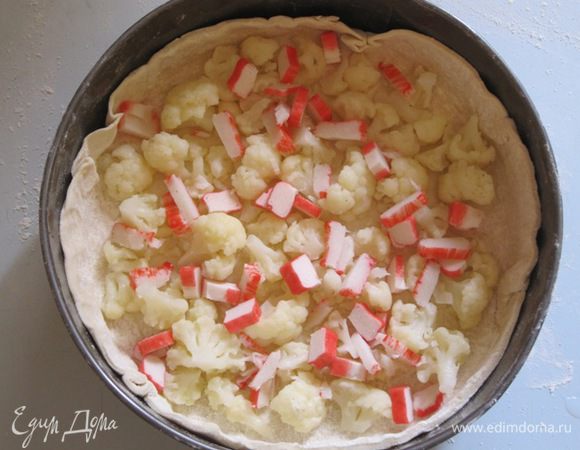 Слоеное тесто раскатать, уложить в смазанную маслом форму. На тесто выложить нарезанные крабовые палочки и цветную капусту.