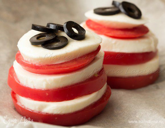 На ломтик помидора выложить ломтик моцареллы, потом снова томат и снова сыр. Оптимально в каждой башенке сделать по 3 томатно-сырных яруса.