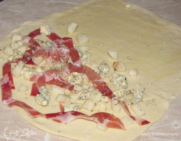 Когда тесто подойдет, разделить его на 4 равные части. Каждую часть теста раскатать в овальный пласт и с помощью кисточки смазать оливковым маслом. На одну половину выложить груши и бекон, добавить немного раскрошенного сыра, посыпать сухим тимьяном и перцем.  