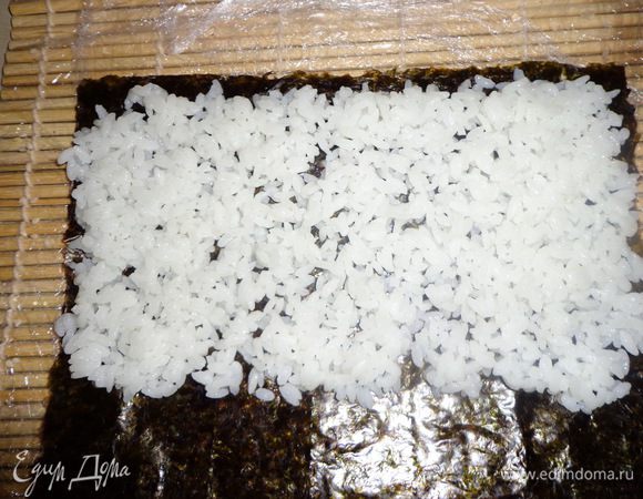 Для сворачивания суши вам понадобится бамбуковая циновка – макису и мисочка с холдной водой, для того, чтобы рис не прилипал к рукам
На макису кладем лист нори пупырчатой стороной вверх. 
Выкладываем руками, смоченными в холодной воде, рис. Необходимо руки смачивать каждый раз, прежде чем взять новую порцию риса. 
Равномерно распределяем рис по нори, оставляя один край свободным. 
Посыпаем рис кунжутом и переворачиваем нори рисом вниз. 