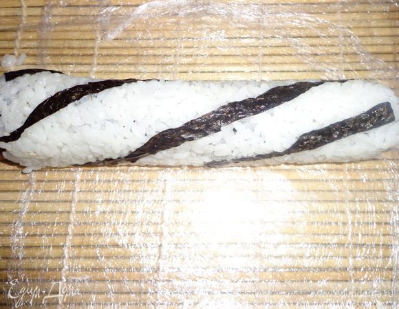 Далее плотно скручиваем, с помощью бамбукового коврика. 
Роллы с семгой я выкладывала на рис, т.е. не переворачивая нории рисом вниз.
Острым нож и нарезаем на 6-8 кусочков. Нож каждый раз необходимо промывать под холодной водой, иначе рис будет прилипать и мешать резать.
