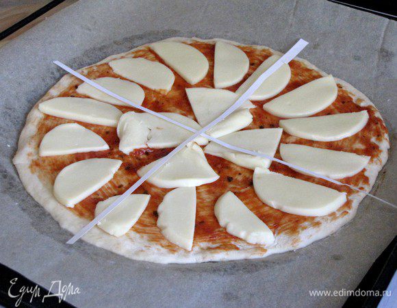Выложить на тесто моцареллу. Из бумаги вырезать две полоски и выложить на пиццу в виде креста, формируя 4 сегмента.