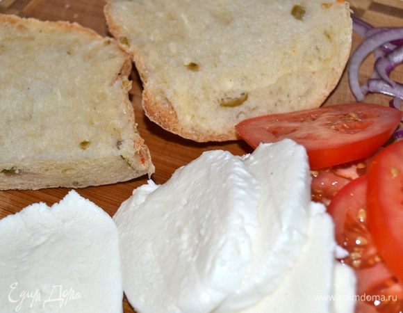 Лук нарезать тонкими полукольцами. Из чиабатты вырезать кружки по размеру помидоров. Помидоры и моцареллу нарезать тонкими кружками.