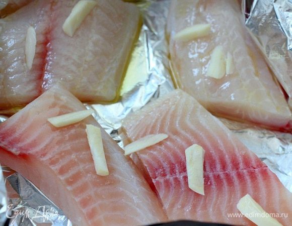 Кусочки тилапии солим, перчим, взбрызгиваем оливковым маслом, посыпаем нарезанным чесноком.