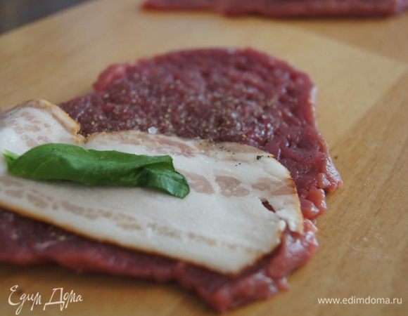 Поперчить каждый кусочек, на один край положить полоску бекона, на него листик шалфея. Свернуть кусочек пополам и оставить на доске.