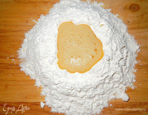 Муку насыпать на деревянную доску небольшой горкой и сделать в центре углубление, влить туда смесь из взбитых яиц, соли и оливкового масла. 


