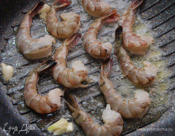 Поставить сковороду-гриль  на средний огонь, добавить по 1,5 ложки сливочного и оливкового масла. Широкой стороной ножа раздавить 1 зубчик чеснока и опустить в сковороду. Туда же отправляем креветки. Обжариваем 1,5минуты с одной стороны.