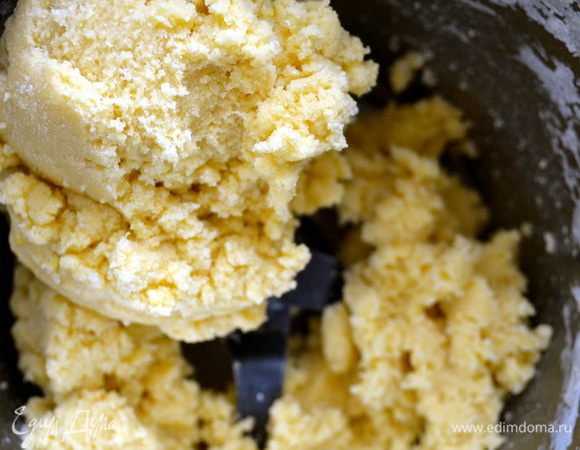 Получившуюся мокрую крошку теста выложить на стол и собрать в шар. Обычно данное тесто достаточно сложно раскатать и выложить в форму, даже после охлаждения в холодильнике. Оно ломается. Можно попробовать сначала охладить тесто в холодильнике, а после раскатать его между двумя листами пекарской бумаги.