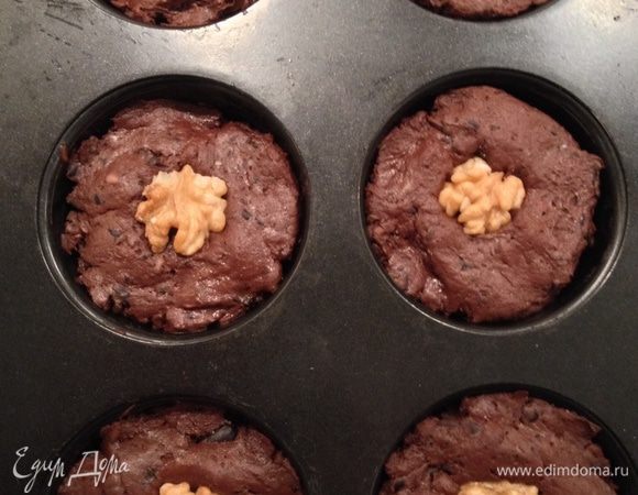 Духовку разогреть до 180 градусов. Форму для маффинов смазать растительным маслом, разложить полученную смесь, немного придавить пальцами, сверху украсить орешком.