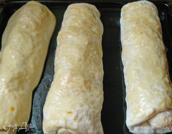 Края теста зажимаем, чтобы при выпекании не выпала начинка, а также зажимаем край теста, образовавшийся при сворачивании, и стараемся уложить рулет швом вниз. Включаем духовку, чтобы нагрелась, а в это время смазываем форму для выпекания маслом. Перекладываем рулеты в форму, смазываем взбитым яйцом и ставим в духовку. 