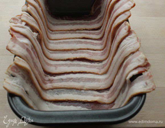 В прямоугольную форму внахлест выложить пластинки бекона, чтобы края свисали.