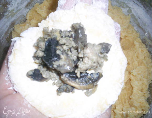 Набираем столовой ложкой картофельную массу, кладем ее в тарелочку с мукой и обваливаем в ней, руки при этом у нас тоже припудрены мукой. Формируем на ладони толстую лепешку.
Кладем на лепешку начинку (примерно столовую ложку) и формируем пирожок. Тесто очень мягкое и податливое, следите, чтоб оно не порвалось. Таким образом формируем остальные пирожки, выкладываем их на поверхность, обильно посыпанную мукой, швом вниз.