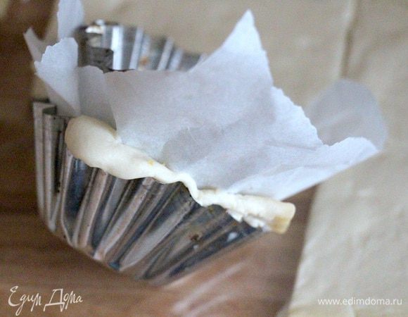 Квадратики слоеного теста положить в смазанные маслом формочки для кексов. Накрыть пекарской бумагой и поставить внутрь еще одну формочку для кекса, прижав таким образом тесто. 