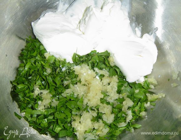 А мы приготовим намазку, для этого чеснок измельчаем с помощью пресса, зелень мелко нарезаем и соединяем все со сметаной.