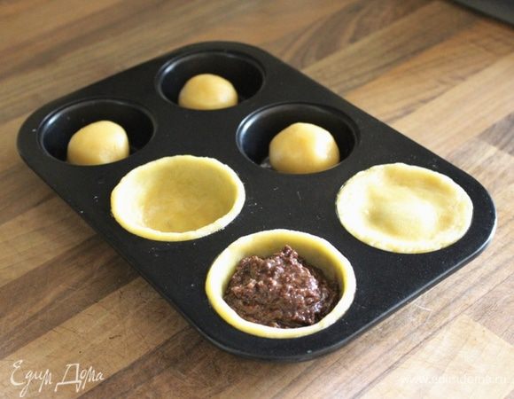 Небольшие формы для маффинов (у меня формы по 100 мл каждая) смазать маслом и припудрить мукой (кроме силиконовых и антипригарных). В каждое углубление уложить по кусочку теста, размером с шарик для пинг-понга. Пальцами распределить тесто по дну и стенкам формы. В каждую розетку положить по 2 ч.л. теста (или заполнить розетки на 3/4 объёма). Оставшееся тесто раскатать на присыпанной мукой поверхности в пласт, толщиной 3 мм. Вырезать из теста круги, совпадающие по диаметру с розетками. Накрыть розетки кругами теста и немного защипать края. Выпекать бокканотти около 20-25 минут при 180*С.