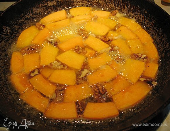 Когда карамель немного потемнеет в нее уложим тыкву и в промежутки кусочки орехов. Сковороду прикроем фольгой и поместим в разогретую до 200 градусов духовку на 15 минут.  Вынуть сковороду с тыквой из духовки, дать немного остыть. 