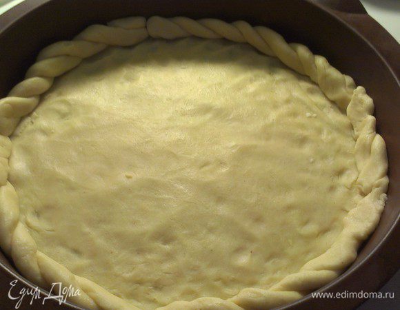 Между двумя пергаментными листами раскатываем тесто по диаметру формы (у меня силиконовая форма диаметром 28 см.).
Из остатков теста формируем бортик. Я оформила в виде косички.