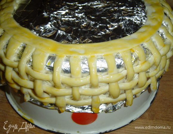 Пока торт находится под прессом займемся украшением. Прежде всего изготовим корзинку, для этого слоеное тесто нарезаем полосками, 4 длинных, а остальные нарезаем по высоте торта + 2 см. Берем миску диаметром на 2-3 см больше, чем диаметр торта, накрываем фольгой, сверху крепим короткие полоски, а между ними в шахматном порядке пропускаем длинные полоски и скрепляем концы. Одну длинную полоску немного раскатываем, с одной стороны немного смачиваем водой, накладываем на закрепленные короткие полоски и немного прижимаем.