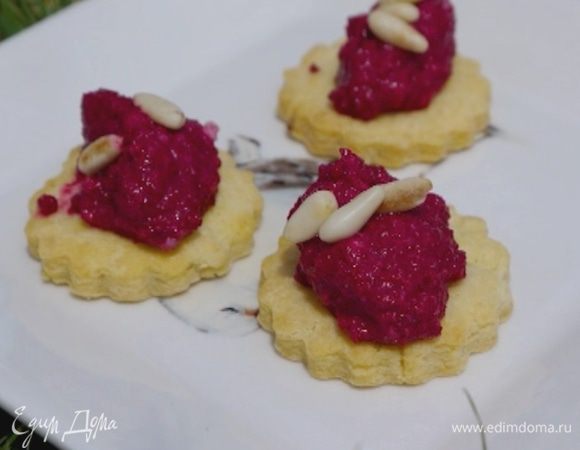 На сырное печенье выложить соус песто и присыпать оставшимися орехами.