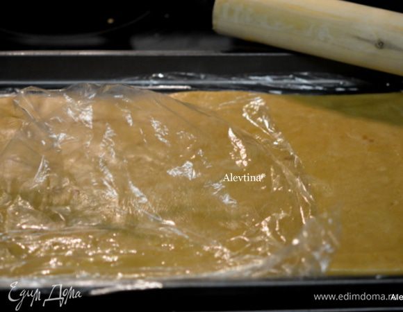 На противень 22 на 30 см разложить пищевую пленку или бумагу для выпечки. Выложить тесто на пленку и раскатать его по размеру противня аккуратно не тонко, а также используем пленку на поверхности теста, так будет легче раскатывать. Тесто послушное.