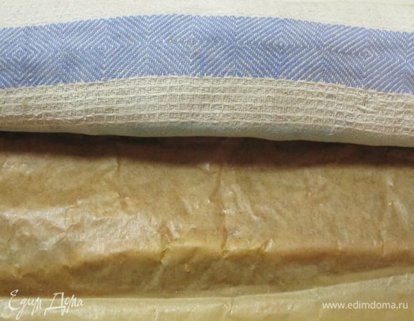 На стол выложить полотенце, равномерно посыпать его 2 столовыми ложками сахарной пудры. Вынуть противень из духовки, пройтись ножом по краям коржа и аккуратно переложить его пергаментом кверху на полотенце. Не снимая пергамента, осторожно скатать корж в рулет и дать остыть.