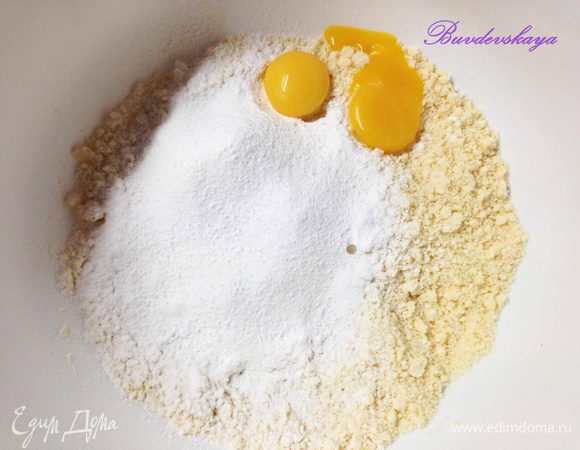 Переложить крошку в большую миску, просеять сахарную пудру, ванилин, желтки и соль.  Тщательно перемешать (довольно быстро), чтобы получилось гладкое, эластичное тесто. При необходимости добавить  немного холодного молока  (примерно 2 ст.л.) 