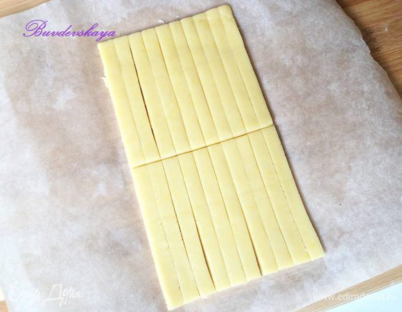 Достать тесто из холодильника, разрезать на 2 части и вторую часть убрать обратно в холодильник, так как лучше работать с холодным тестом.  Раскатать тесто толщиной примерно в 1 см, нарезать при помощи линейки на полоски длиной 20 см и шириной  1 см. Затем разрезать полоски на пополам, чтобы получились палочки длиной 10 см.