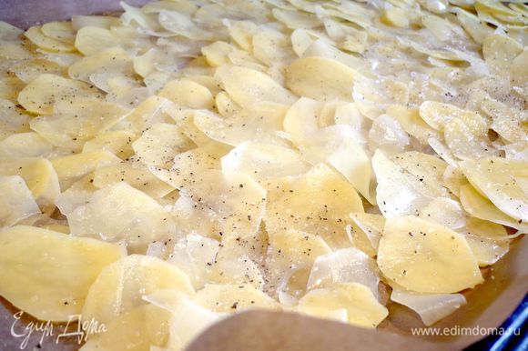 Выкладываем на противень, выстеленный смазанной оливковым маслом пекарской бумагой, внахлест. У нас на это уйдет примерно 2/3 всего картофеля. Посыпаем солью и перчим.