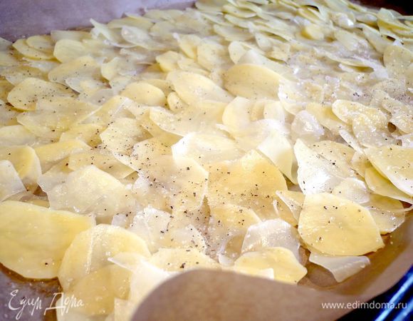Выкладываем на противень, выстеленный смазанной оливковым маслом пекарской бумагой, внахлест. У нас на это уйдет примерно 2/3 всего картофеля. Посыпаем солью и перчим.