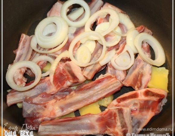 Масло это (граммов семьдесят – максимум) выкладываем в кастрюлю. На самое дно. Кастрюлю мы взяли чугунную, толстодонную и массивостенную. 
Поверх кусочков масла уложить надо ребрышки, а потом слой лука.
