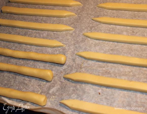 Выложить заготовки на противень, застеленный пергаментной бумагой, отрезать уголки полосок острым ножом так, как будто заточили карандаши.