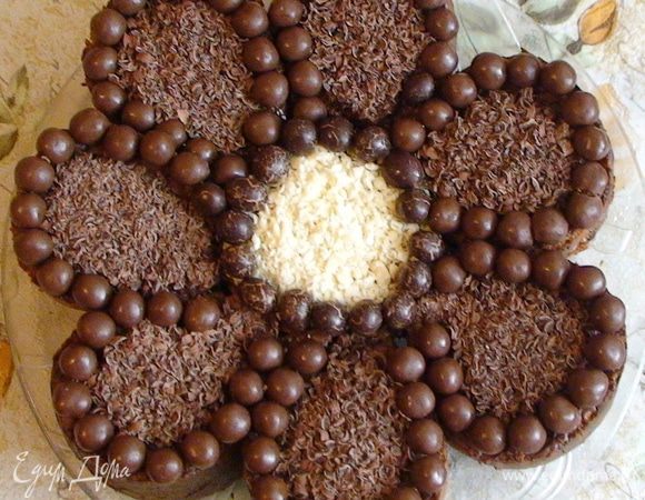 Выложить каждый лепесток и серединку торта маленькими круглыми конфетками (у меня рисовые шарики в шоколаде). Присыпать серединку тертым белым, а все лепестки тертым черным шоколадом. Если есть разноцветная кокосовая стружка – можно вместо шоколада каждый лепесток оформить разным цветом – получится «цветик-семицветик». Или украсить любым другим способом – по вашему вкусу и фантазии.