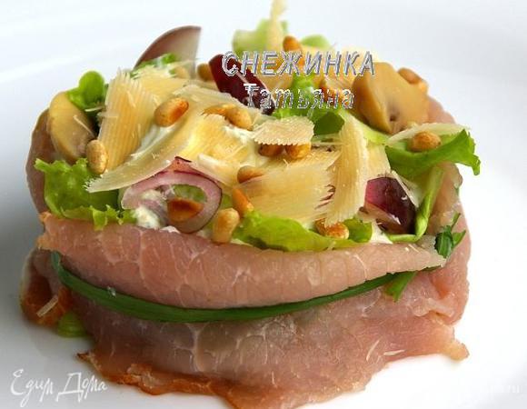 Оборачиваем «конструкцию» ломтиками окорока (по 3 на порцию), чтобы салат держал форму. Обвязываем пером зелёного лука. Сверху обильно посыпаем хлопьями сыра Джюгас и кедровыми орешками. 