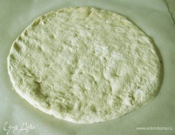 Разбухший шарик теста размял руками в блин толщиной в мизинец, переложил на противень, застеленный пекарской бумагой, и обмял ладонями, придав форму круга.