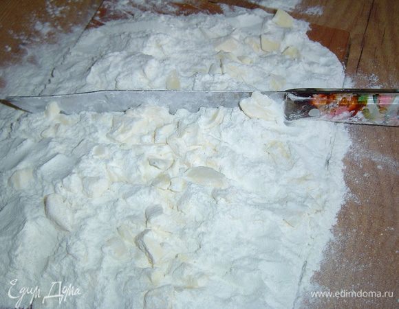 Начинаем процесс с приготовления теста. Холодное сливочное масло нарезаем крупными кусками, сверху насыпаем просеянную муку, щепотку соли и рубим все вместе ножом до образования не очень мелкой крошки. 