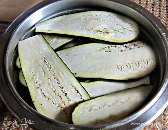 Нарезать баклажаны тонкими продольными пластинами толщиной 5 мм. Натереть солью и дать постоять 15 мин. После этого слить образовавшуюся горечь и промыть баклажаны под холодной водой, обсушить.