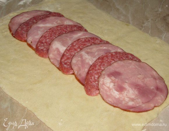 Подошедшее тесто разделить на две части. Каждую часть раскатать в прямоугольник толщиной примерно 0,5 см. По центру выложить ветчину, чередуя с салями.