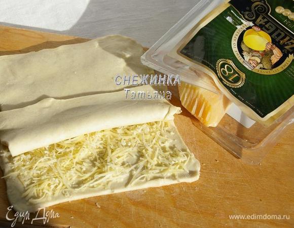 Сыр Джюгас натираем на мелкой тёрке. На одну половину теста распределяем сыр. Накрываем второй половиной. Раскатываем тесто в таком виде снова в прямоугольник по размеру, как в первый раз.