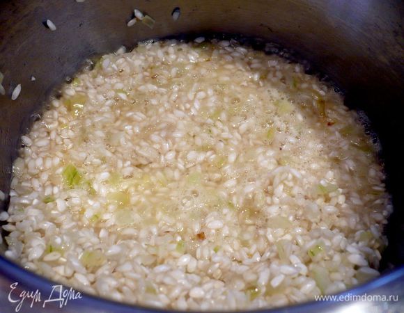 В сотейник с поджаренным луком всыпаем рис и обжариваем его почти до прозрачности на среднем огне, вливаем вино, при этом не забываем хорошо помешивать ризотто. 