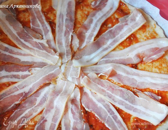 Выложить начинку. Для этого ошпарить помидор, разрезать, удалить косточки. Измельчить его в блендере. Добавить соль, травы и масло. Перемешать и смазать тесто. Уложить полоски бекона.